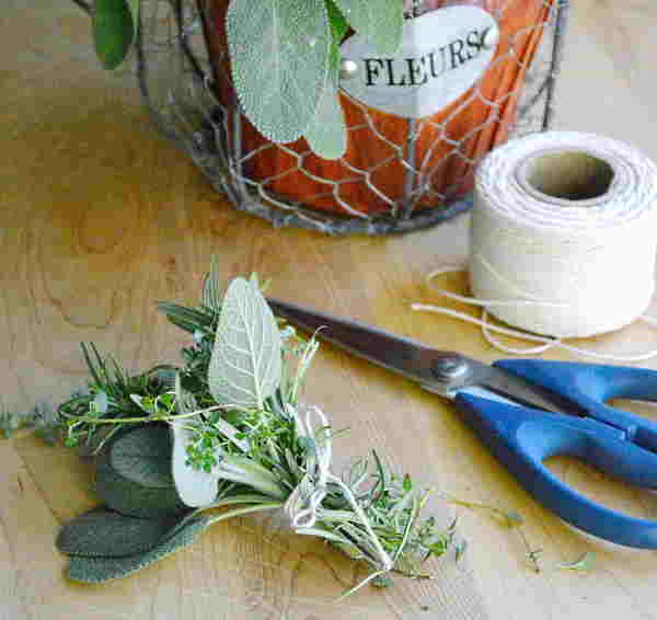 A bunch of fresh herb sprigs and leaves tied together, with a pair of of blue handled scissors and a ball of string beside them.