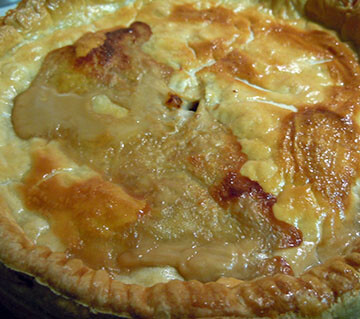 A golden beige and brown Pork, apple and chestnut pie in a pie tin.