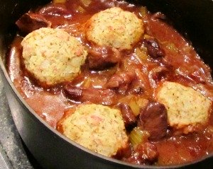A casserole dish filled with chunks of venison meat, carrots, celery, onions, and white dumplings.