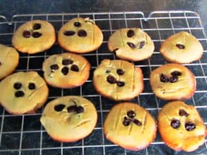 Eleven round beige Breton Cookies sprinkled with dark currents, sitting on a cooling rack.