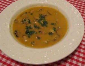 White soup bowl full of yellow broth with beige mussel pieces and green parsley. 