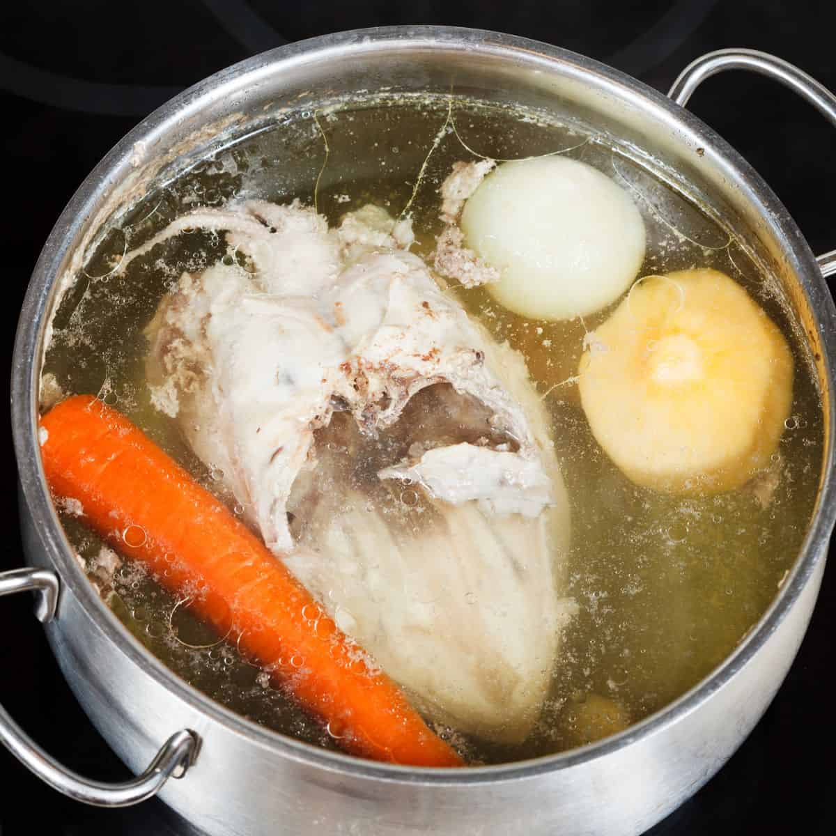 Metal cooking pot full of chicken, onion, parsnip and carrot in cooking broth.