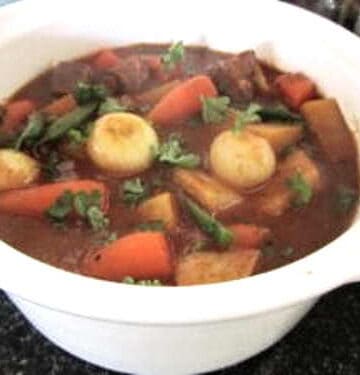 White bowl with lamb, carrots, and many other colorful vegetables.