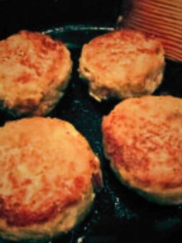 Four round golden brown cakes in a black frying pan.