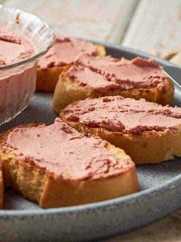 Grey stone plate with slices of oval toast, buttered with smooth brown pate.