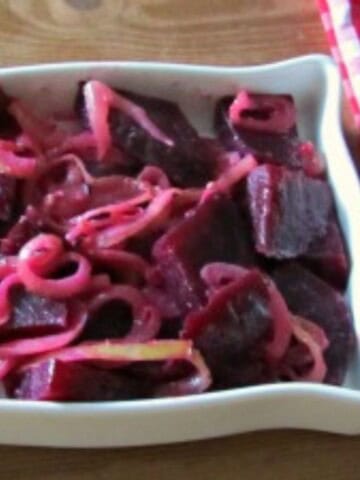 Beets and onions in a square white dish on a brown surface with red and white napkin.