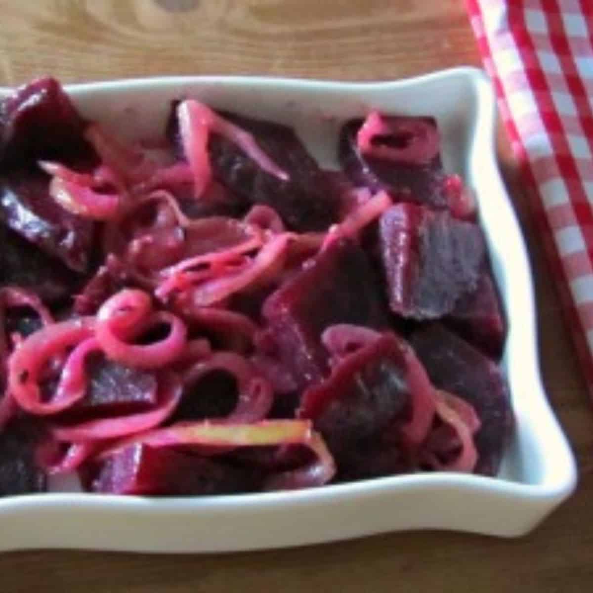 Beets and onions in a square white dish on a brown surface with red and white napkin.