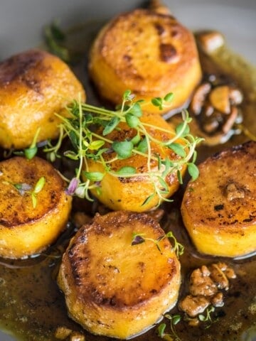 Specially shaped potatoes crisping up in a pan with butter, thyme, garlic, and pepper.