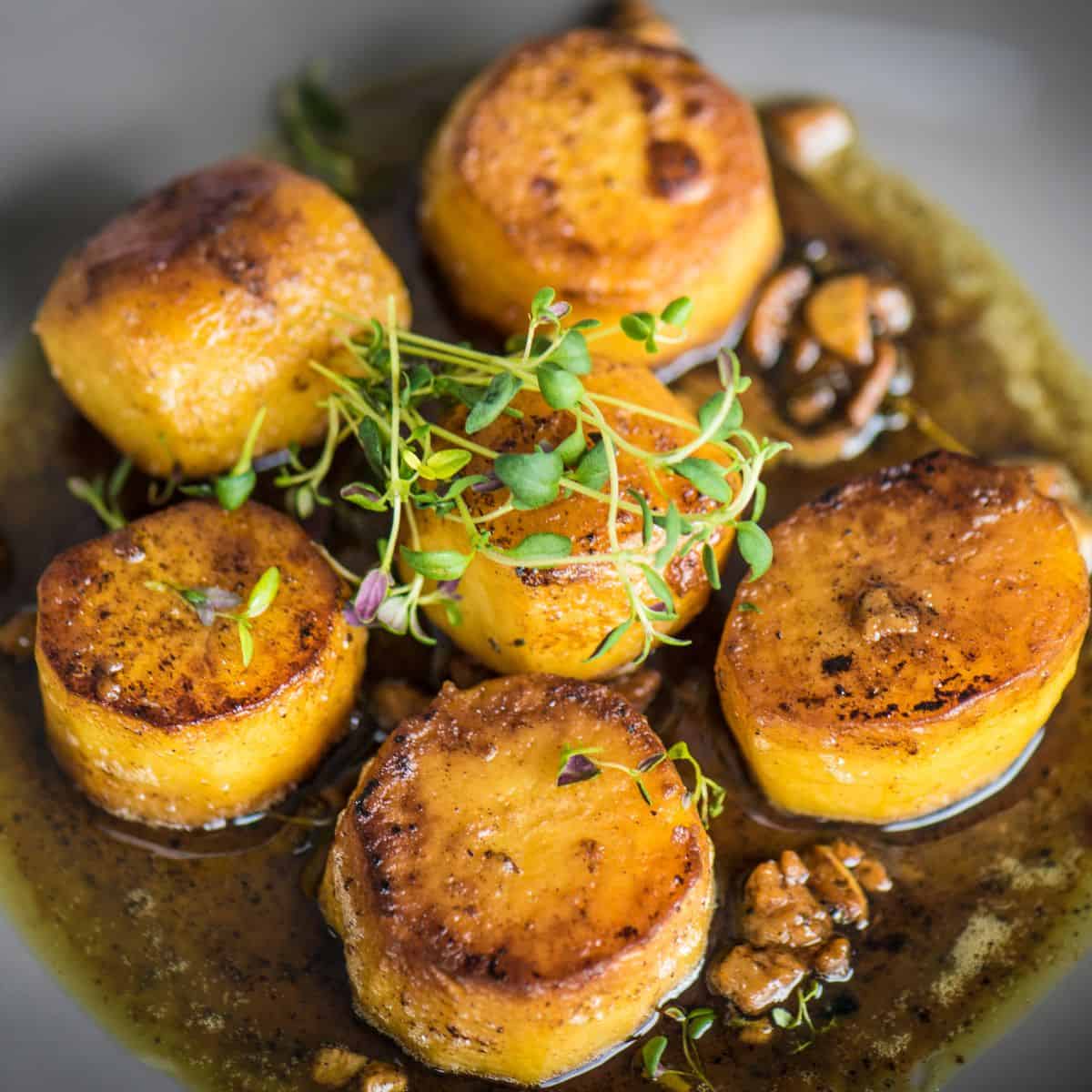 Specially shaped potatoes crisping up in a pan with butter, thyme, garlic, and pepper.