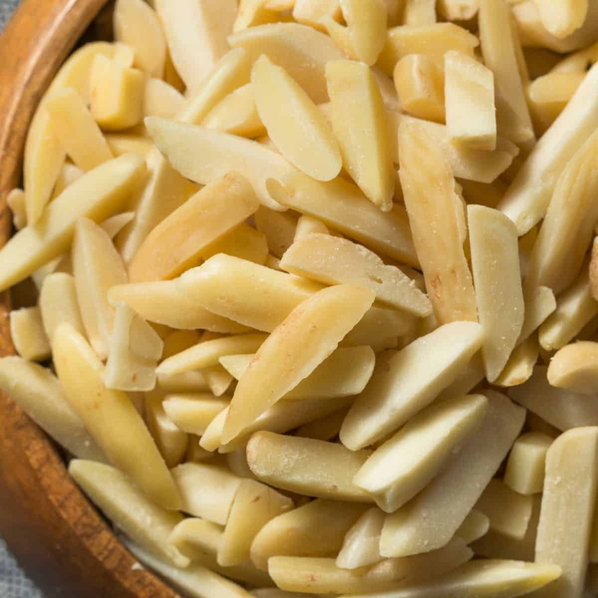 A wooden bowl full of cream colored almonds sliced into slivers.