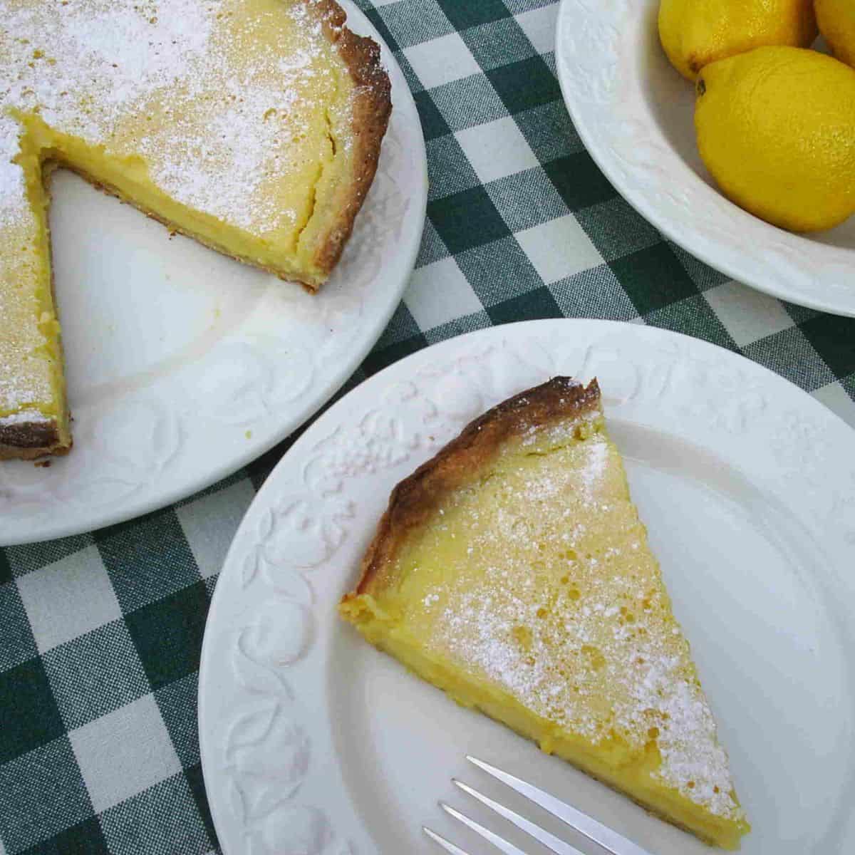 A slice of yellow lemon tart, sprinkled with white icing sugar with a brown crust.