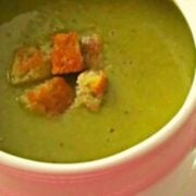 White soup bowl with green creamy pea soup topped with golden croutons.