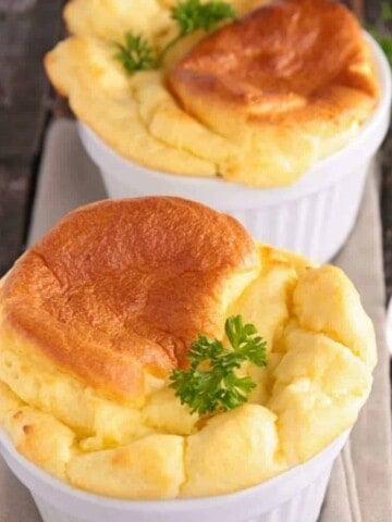 Two white oven pots with fluffy yellow and light brown egg souffles with parsley sprigs.