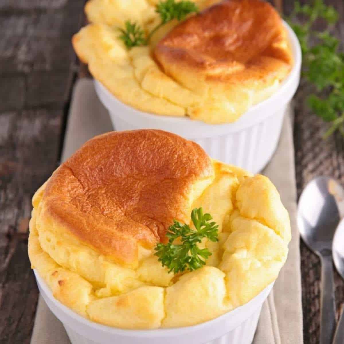 Two white oven pots with fluffy yellow and light brown egg souffles with parsley sprigs.