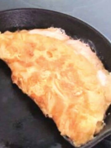 A frying pan with a golden yellow and brown omelette with orange cheese leaking out.