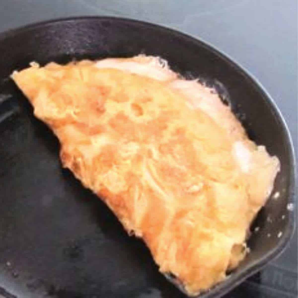 A frying pan with a golden yellow and brown omelette with orange cheese leaking out.