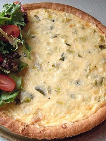 A round dish like a pizza but yellow in the center with green bits and light brown crust and a green lettuce and red tomato salad on one edge.