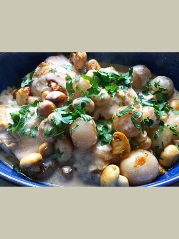 Chicken pieces, mushrooms in cream sauce in a blue bowl.