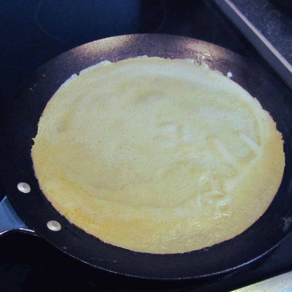 Black crepe pan with a white crepe cooking in it.