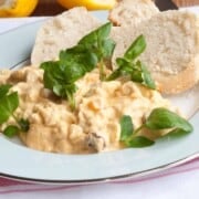 Chicken salad with basil garnish and white bun on white plate.