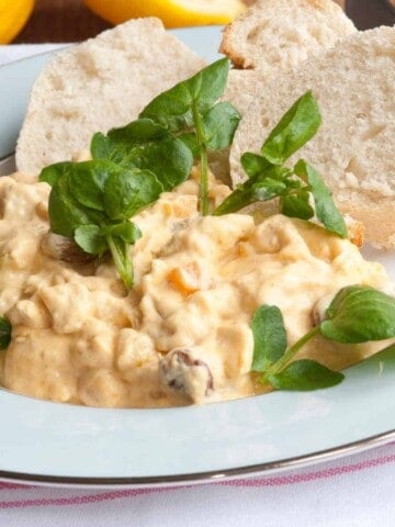 Chicken salad with basil garnish and white bun on white plate.