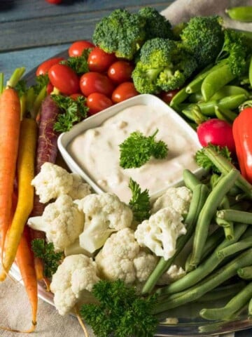 White plate filled with assortment of vegetables and a white bowl of dip.