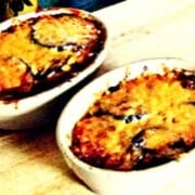 Two white baking dishes with eggplant covered in cheese.