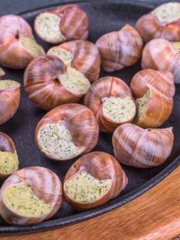 Black plate with snail shells with butter and herbs.