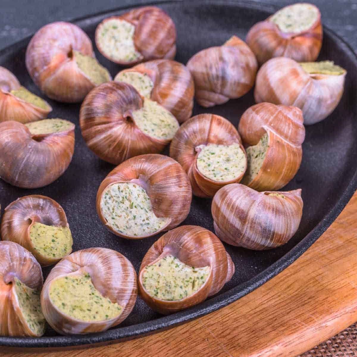 Black plate with snail shells filled with butter and herbs.