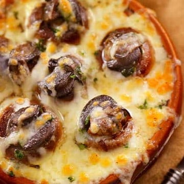 Brown bowl with muchrooms, snails and yellow cheese on top.