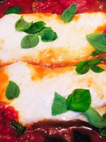 Two pieces of white fish surrounded by red and sprinkled with green leaves.