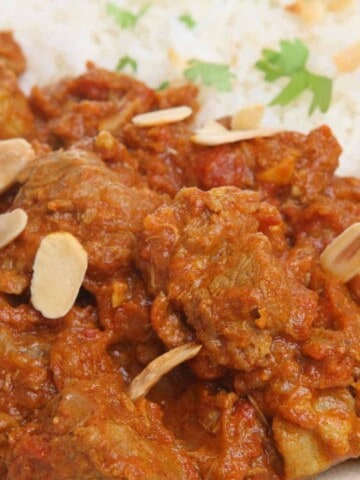 Red meat sauce sprinkled with sliced nuts with rice on the side with parsley.
