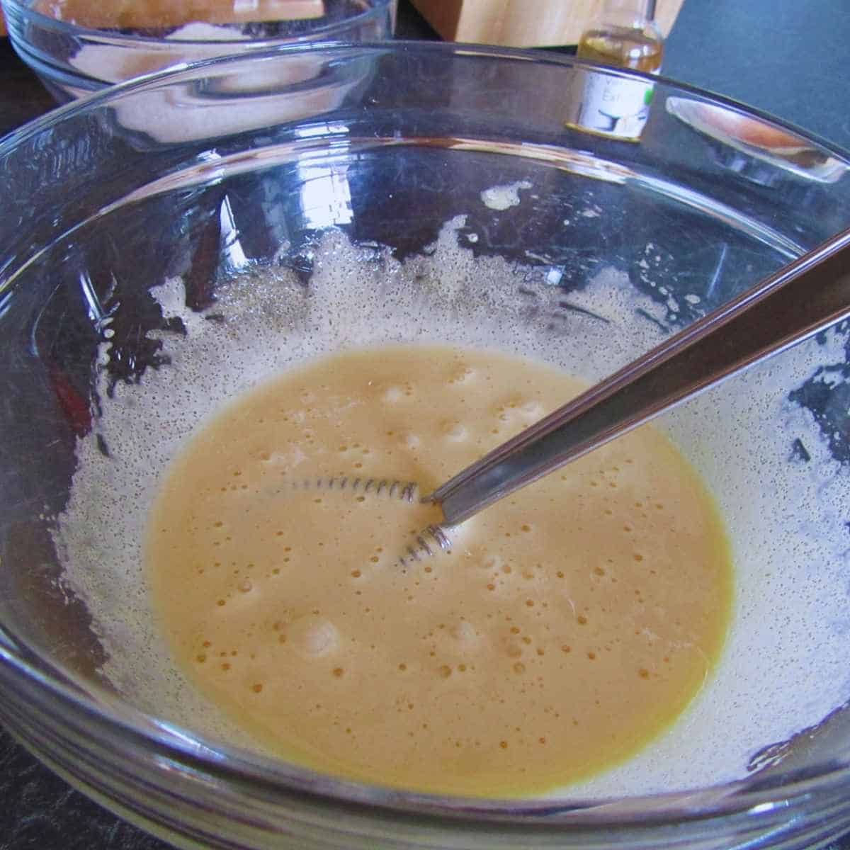 Clear bowl with crepe batter being stirred with a whisk.