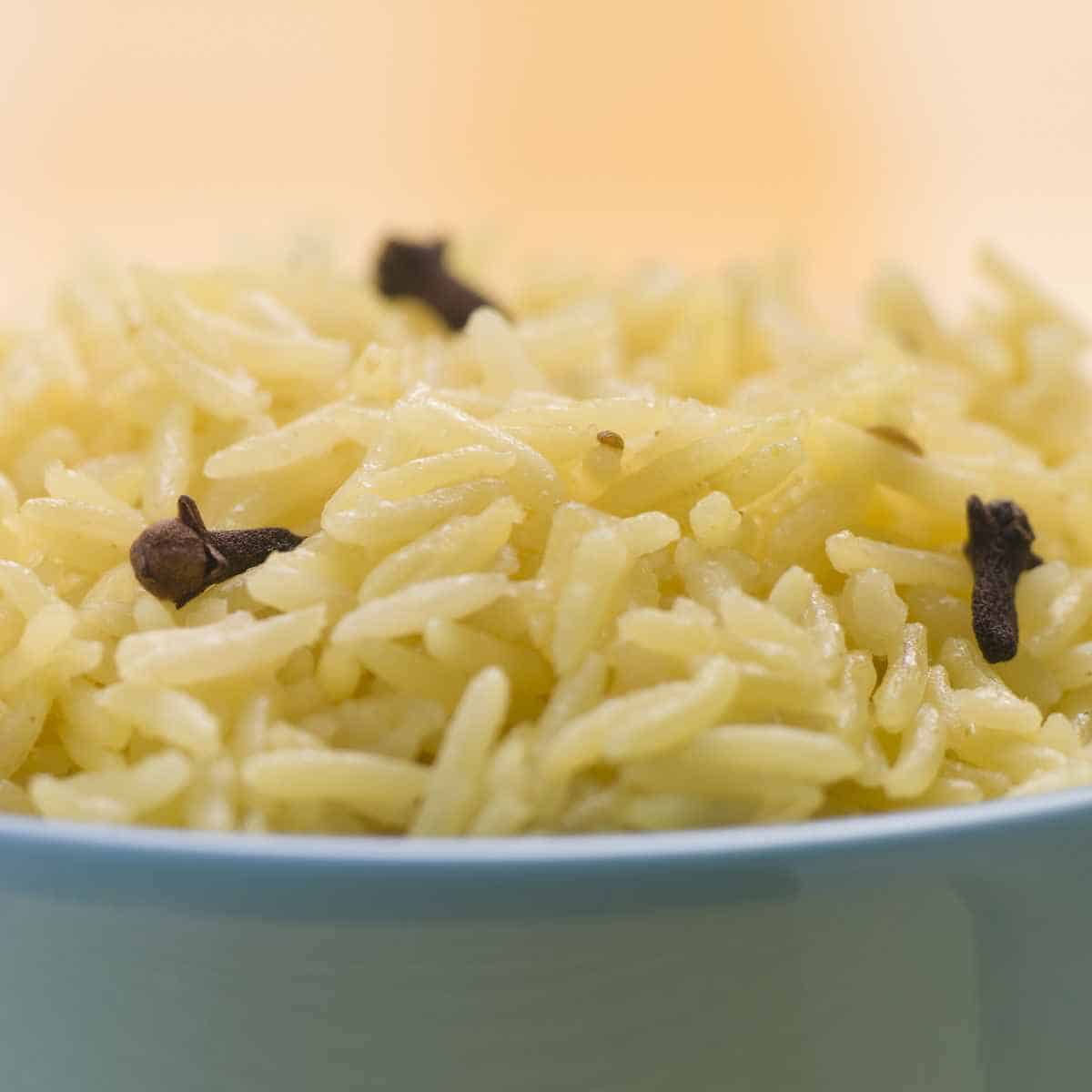 Blue bowl full of rice and 3 cloves on top with pink background.