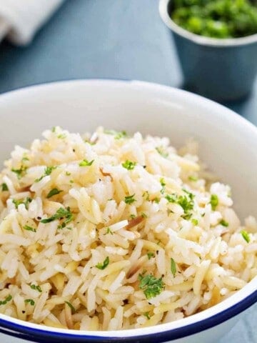 White bowl with white rice and green herbs.