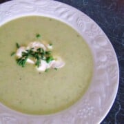 White bowl of yellow soup with dob of sour cream and chives on black counter.