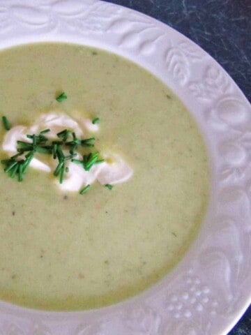 White bowl of yellow soup with dob of sour cream and chives on black counter.