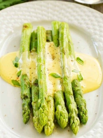 Spears of green asparagus covered in yellow sauce on white oval plate.