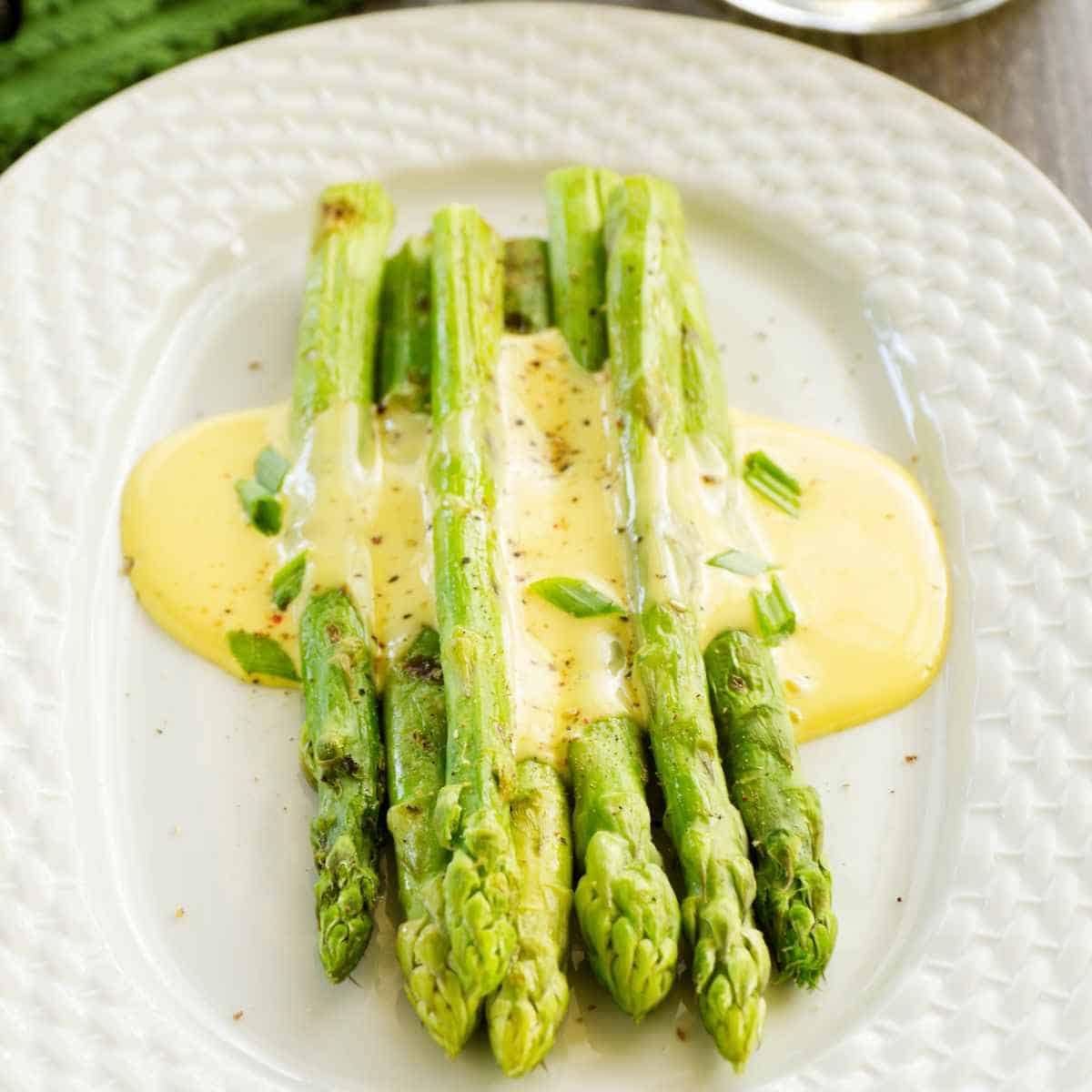 Spears of green asparagus covered in yellow sauce on white oval plate.