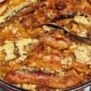 Large red cast-iron pot filled with sausage, beans, bacon, covered with bread crumbs.