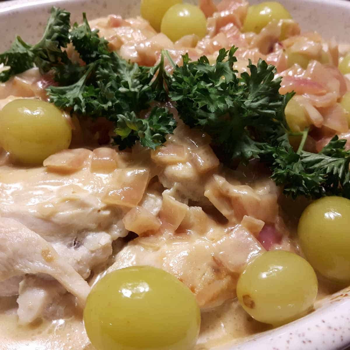 White casserole dish with chicken, grapes, parsley in sauce.