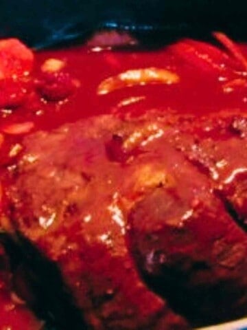 Large slab of red meat, carrots, celery, and onions covered in red tomato marinade.