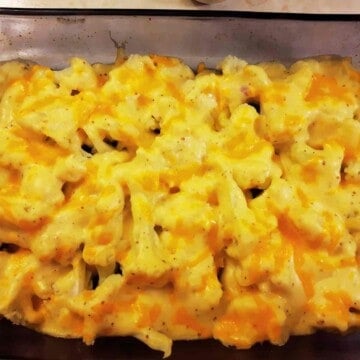 Dark glass oven dish with cauliflower florets covered in yellow cheesy cream sauce.