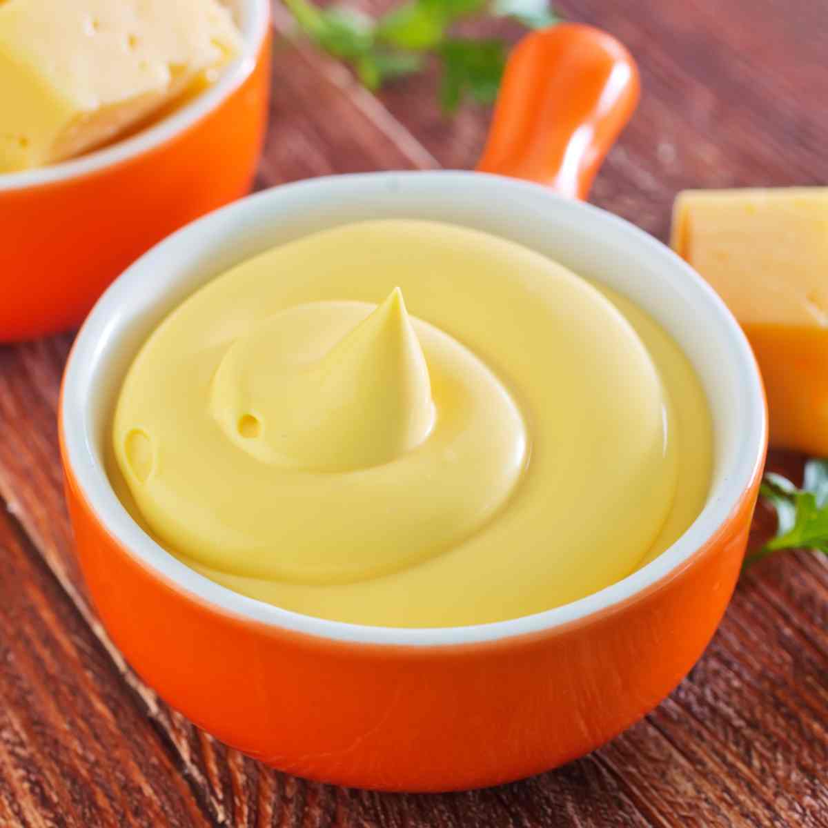 Thick light yellow sauce in an orange dish with chunks of cheese on the side.