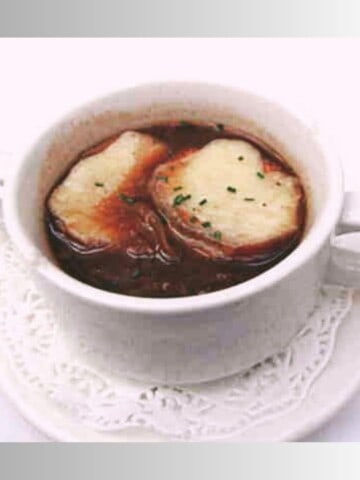 A white soup bowl filled with dark onion soup that has two slices of French bread covered in white melted cheese floating on top.