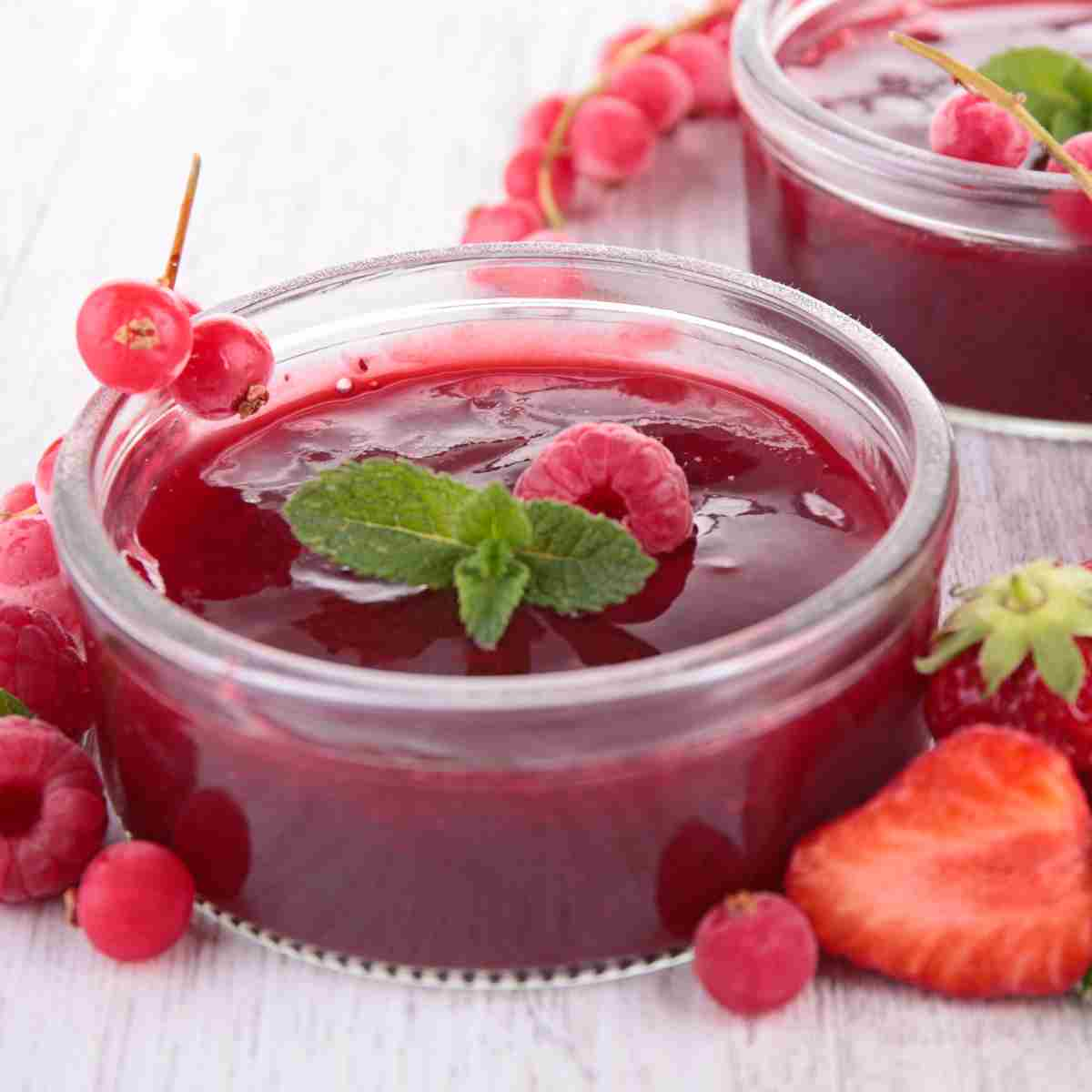 Two clear glass bowls filled with red thick juice, decorated with a raspberry and mint leaf and surrounded with strawberries, raspberries, and round red berries.