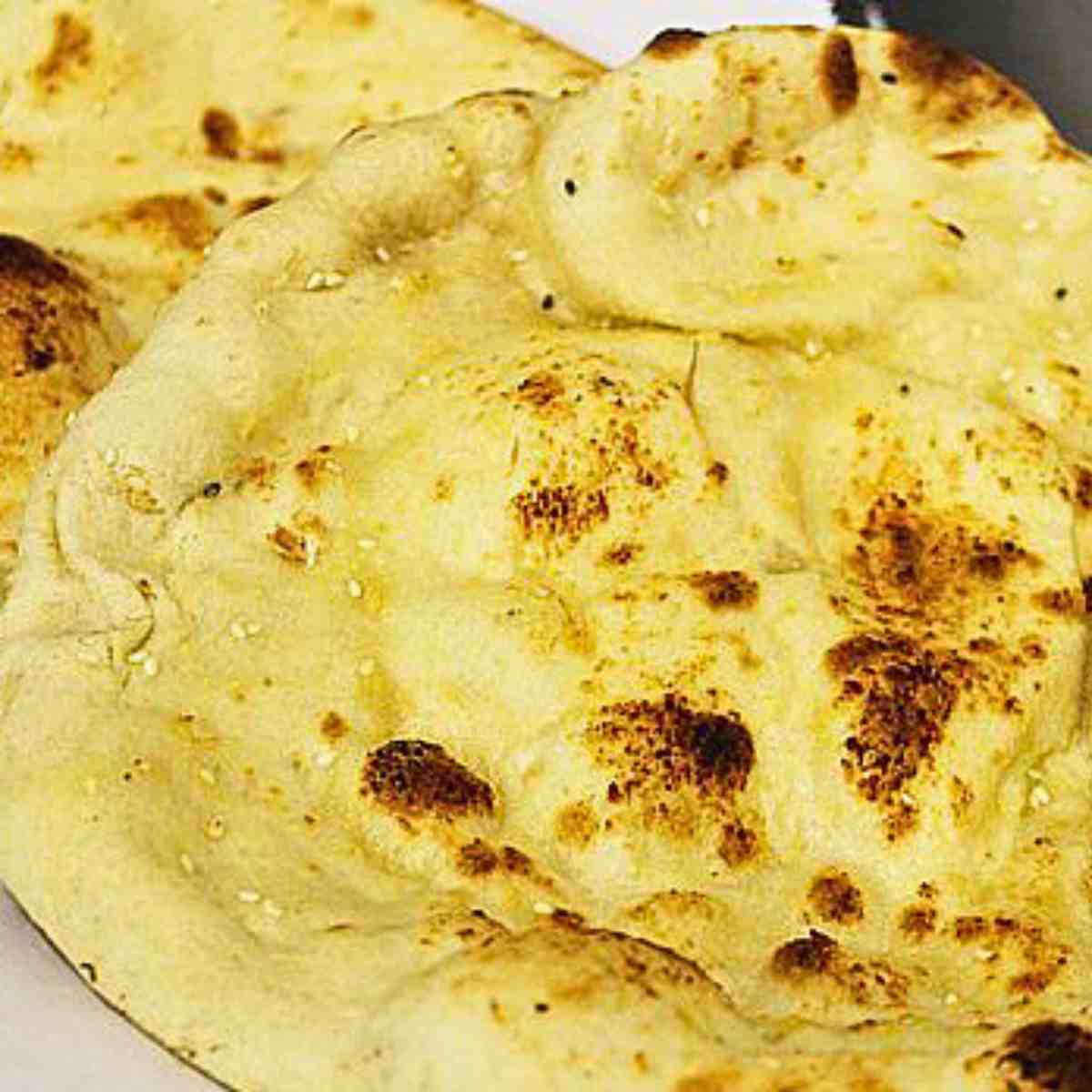 A yellowy, flatbread with puffy spots that are dark brown sprinkled with sesame seed.