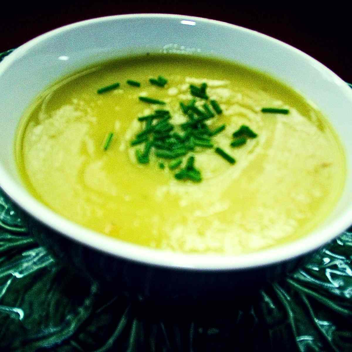 A white soup bowl filled with a creamy light green soup of blended leeks and potatoes sprinkled with dark green chives.