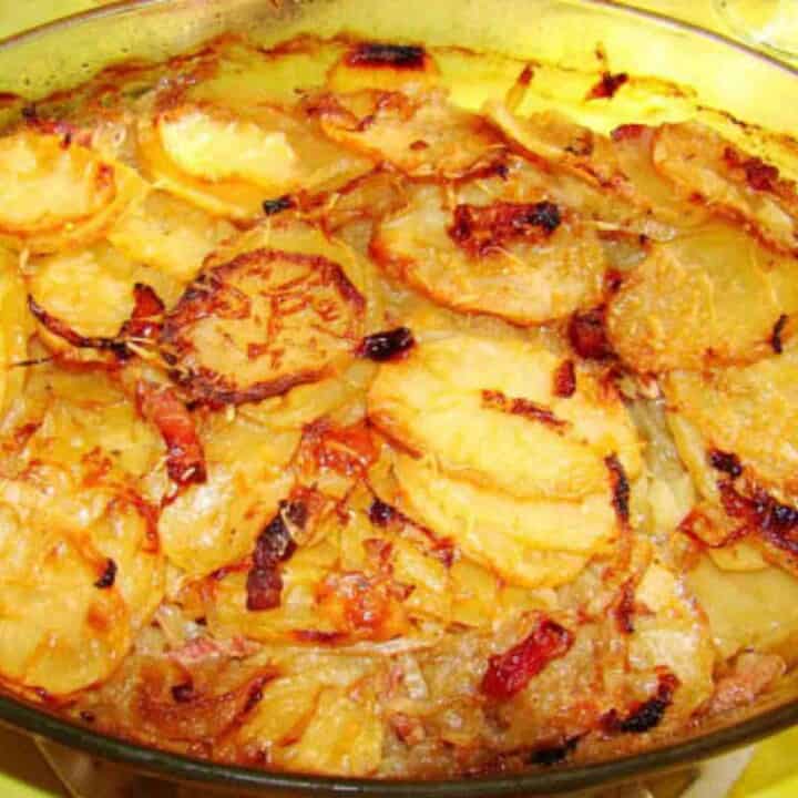 Oven proof dish filled with sliced potatoes and onions topped with green parsley leaves.