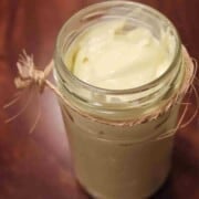A clear glass jar on a pink background full of smooth, creamy, white mayonnaise.